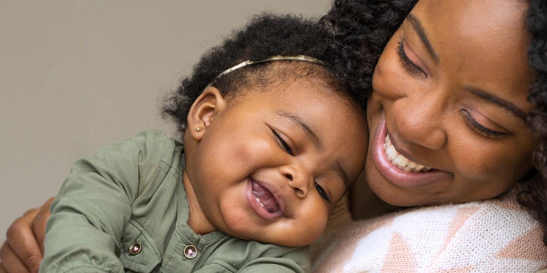 A mother holds her young baby and smiles.