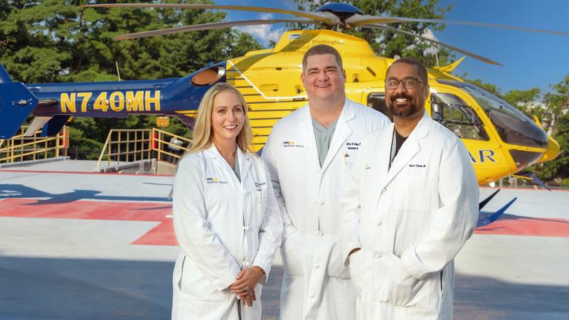 Doctors Taryn Travis, Jeffrey Shupp and Shawn Tejiram pose for a photo on the helipad at MedStar Washington Hospital Center. The helicopter is in the background.