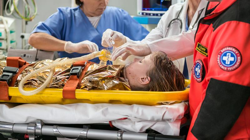 A young child lays on a stretcher while being treated by emergency personnel and first responders.