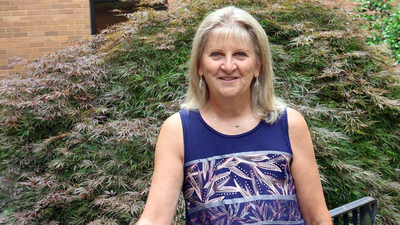 Mary Ellen Gillard stands outside with trees in the background, and poses for a photo after undergoing cancer treatment at MedStar Health.