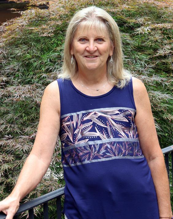 Mary Ellen Gillard stands outside with trees in the background, and poses for a photo after undergoing cancer treatment at MedStar Health.