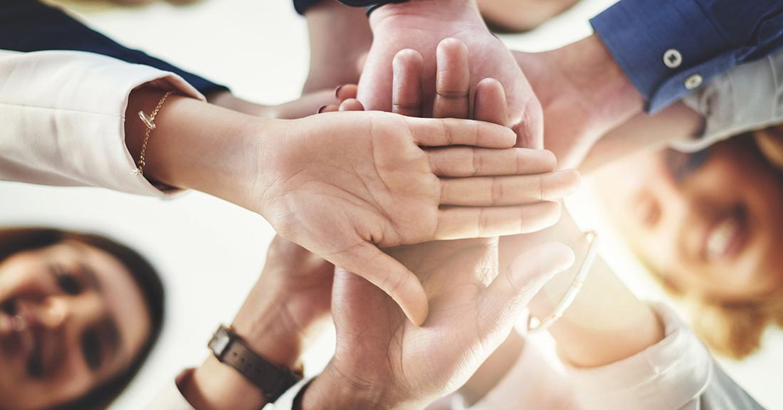 Photo of a group of people with their hands stacked in the middle of a circle, from a low angle.