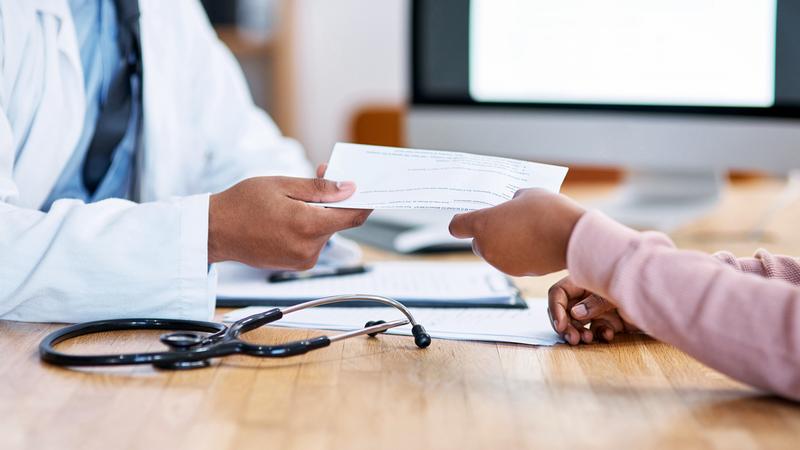 Close up photo of a medical professional handing a piece of paper to a patient in an office setting.
