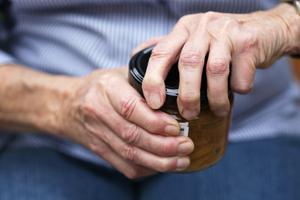 Close up photo of an older woman trying to open a jar, but she has arthritis. Arthritis in the hands causes painful, swollen joints.