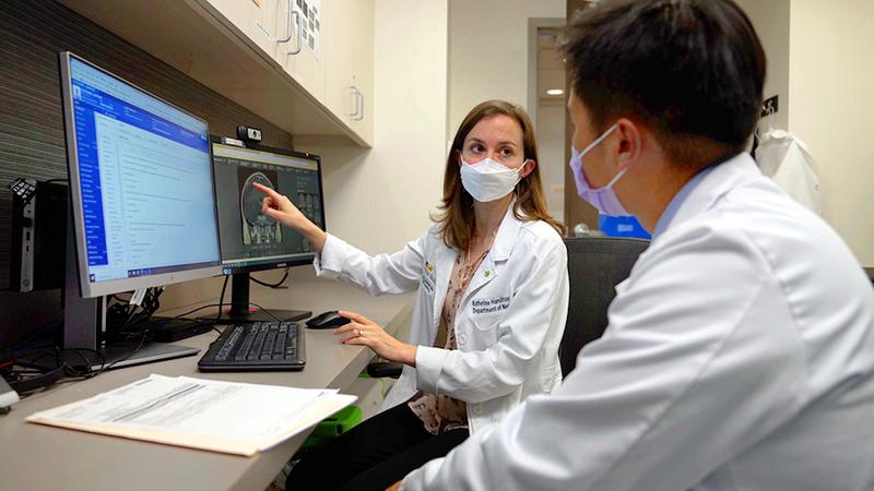 Dr Kathleen Hamilton points to a computer screen while talking to an assistant in an office setting. Both people are wearing masks.