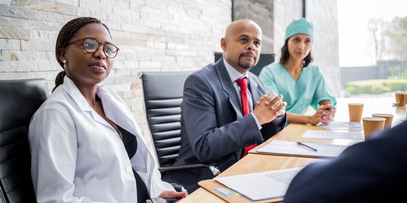 A team of healthcare professionals listen to a speaker during a meeting in a conference room setting.