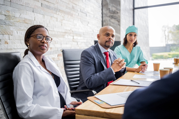 A team of healthcare professionals listen to a speaker during a meeting in a conference room setting.