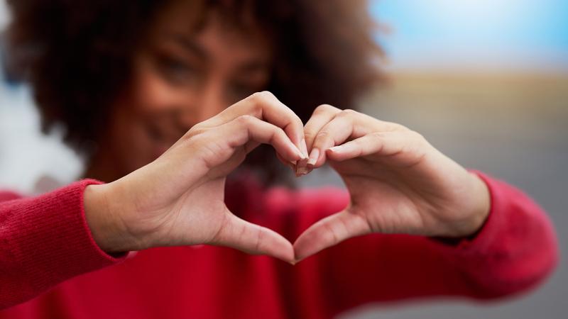 一个女人穿着红毛衣lds her hands in a heart formation.