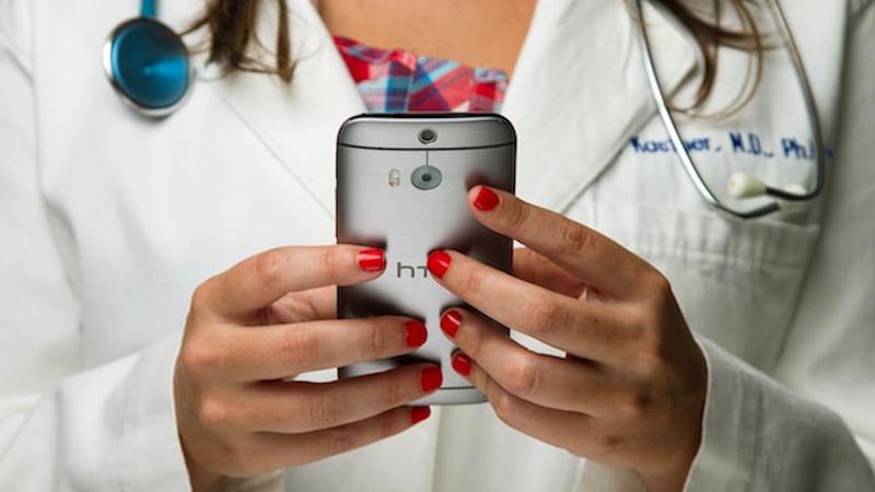 Close up photo of a doctor holding a cell phone and using an app that helps patients with heart failure stay on the proper dosage of lifesaving medications.