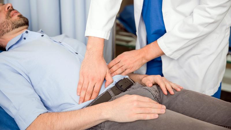 A doctor in white coat palpating belly of man lying on exam table.