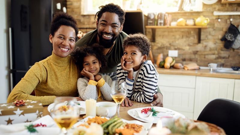 快乐的非裔美国家庭聚在餐桌上吃圣诞午餐，看着相机。