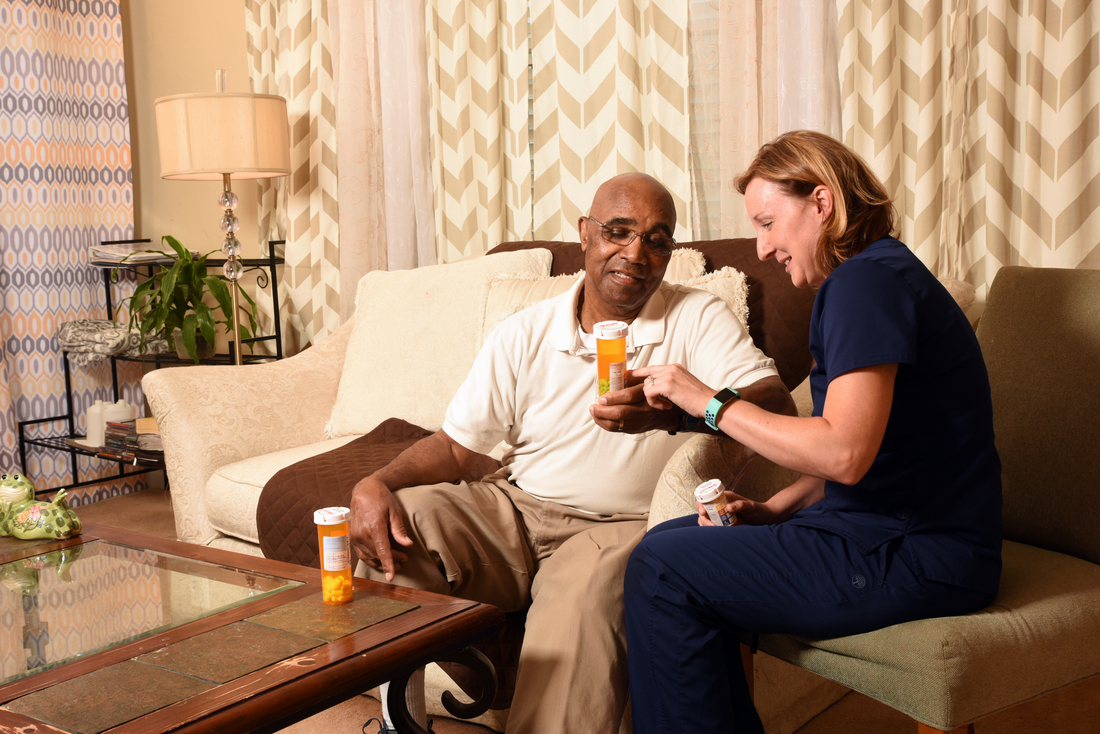 一个穿着蓝色手术服的护士在客厅里和一个男病人谈论他的药物。