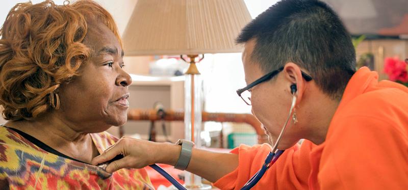 A mature African American female patient has her heart checked by a visiting home care health professional.