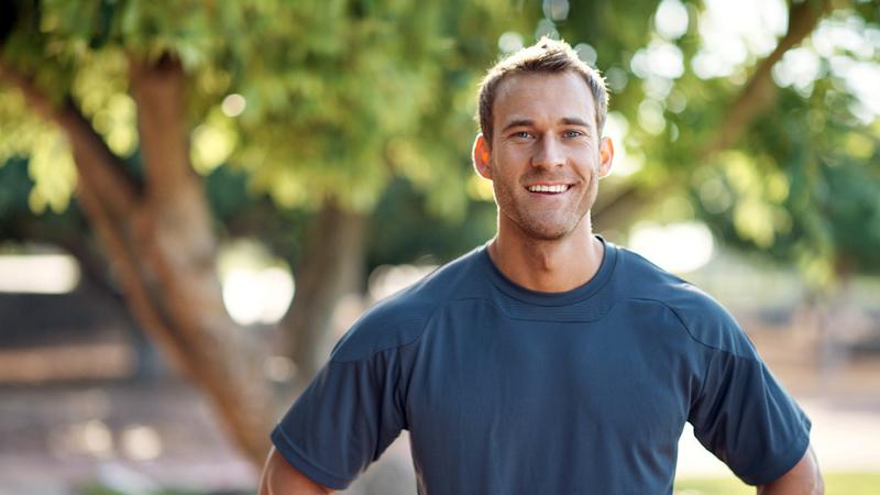 A young athletic man stands outdoors and smiles for the camera.