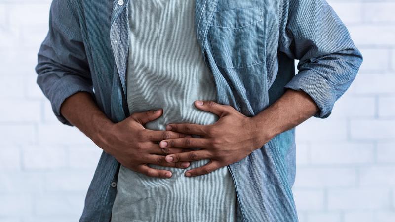 Close up photo of a man clutching his stomach in pain.