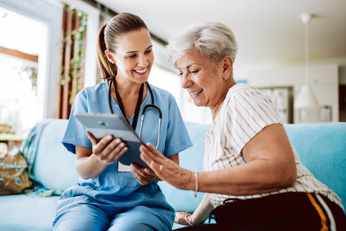 A nurse shows a mature female patient an ipad during a home care visit.