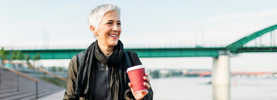 A senior woman holds a cup of coffee as she looks out a river while on a bike ride.