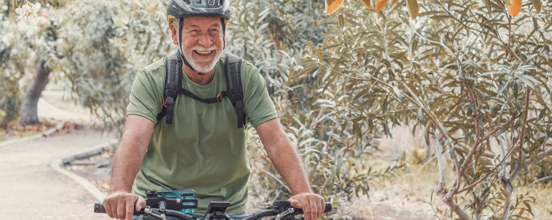 A senior man wears safety gear as he rides his bike through a desert park.