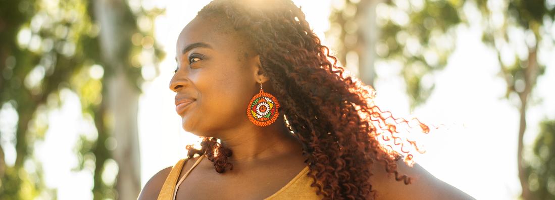 An african american woman stands looking confident outdoors in afternoon sunlight.