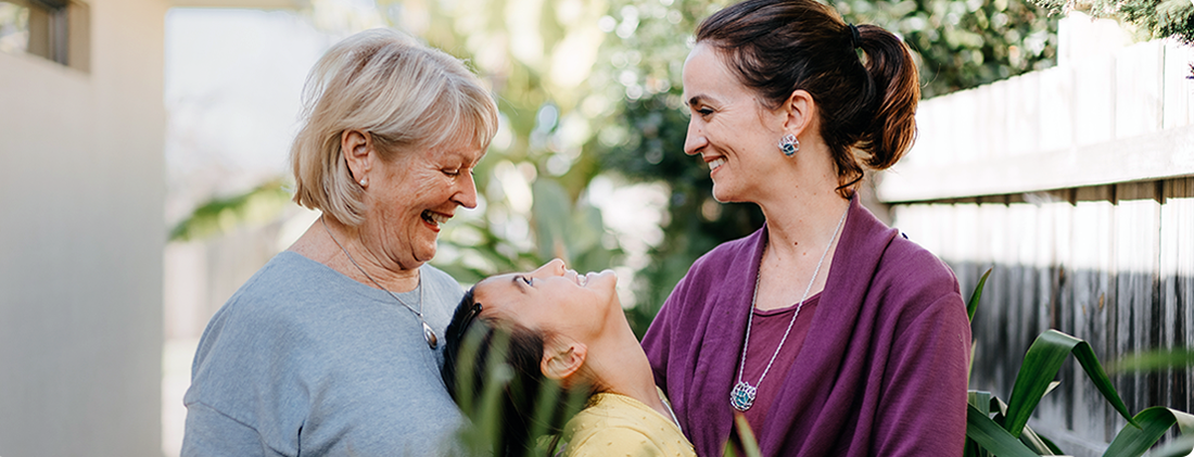 A multi-generational family smiles and laughs together outdoors.