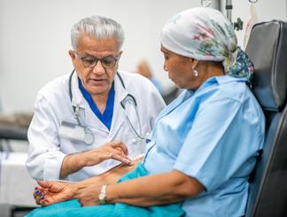 A doctor talks with a patient who is receiving intravenous medications to a patient who is seated.