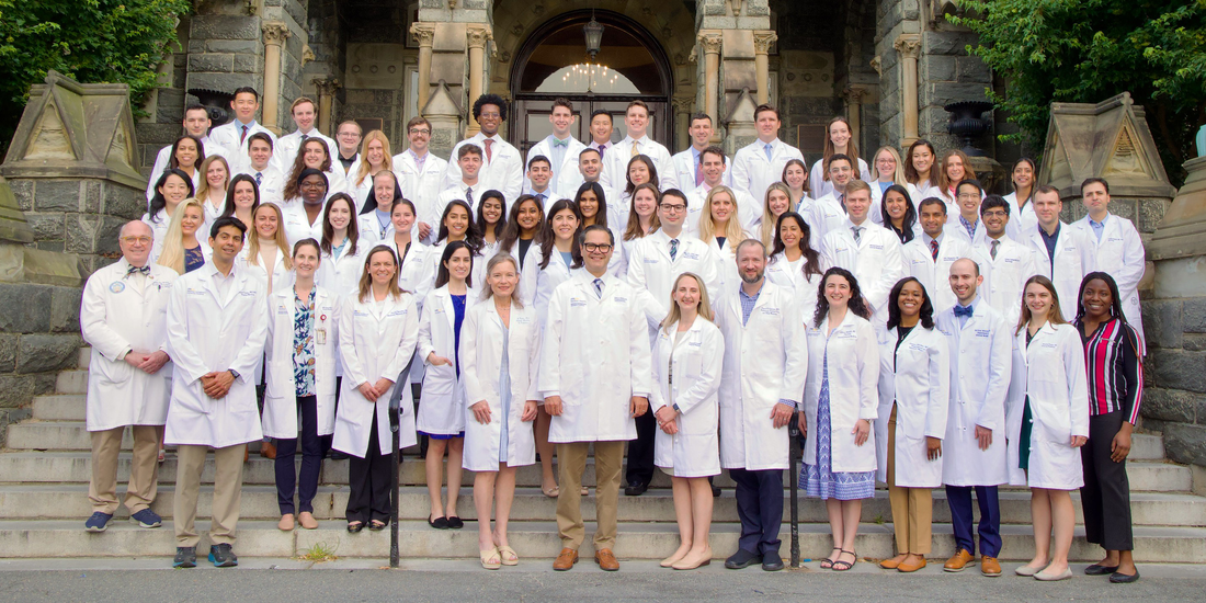 The current class of internal medicine residents at MedStar Georgetown University Hospital stands together on the steps of a historic stone building and pose for a class photo.