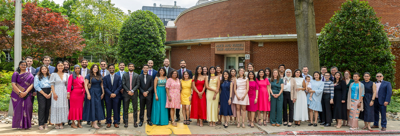 A large group of graduates from the MedStar Health Internal Medicine Residency program stands outside of a red brick building.