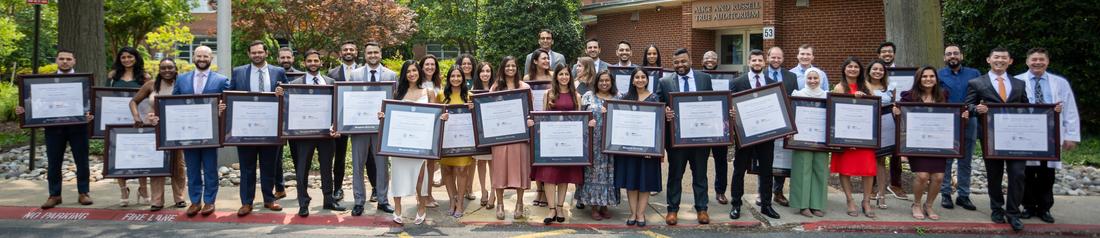 A large group of graduates from the MedStar Health Internal Medicine Residency program stands outside of a red brick building.