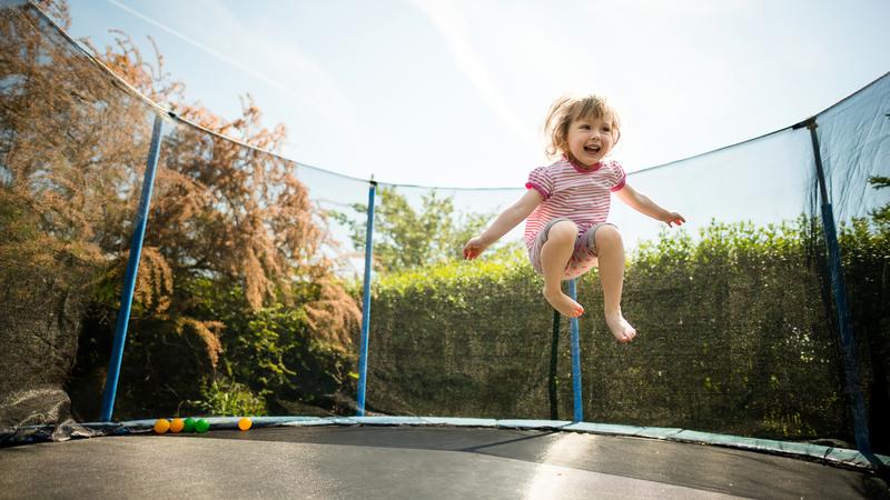 Little child enjoys jumping on trampoline - outside in backyard