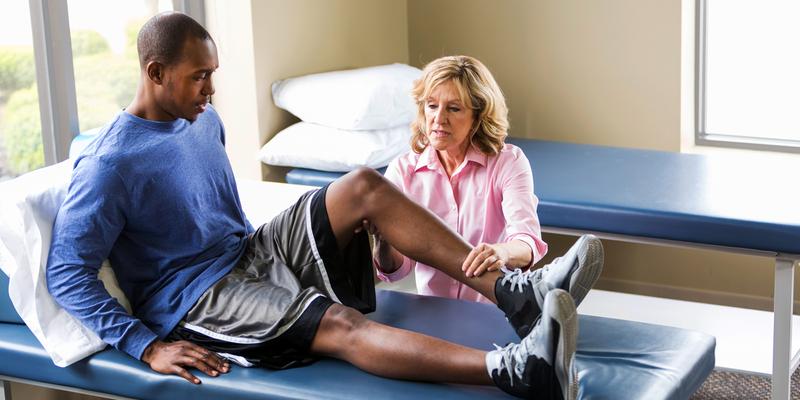 Female physical therapy provider examines athlete's injured knee