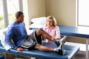 Female physical therapy provider examines athlete's injured knee