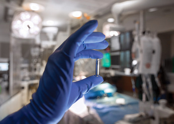 A close up photo of a gloved hand holding a leadless pacemaker device in a clinical setting.