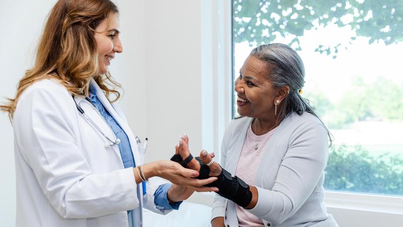 A patient wearing a wrist brace talks with a doctor in a clinical setting.