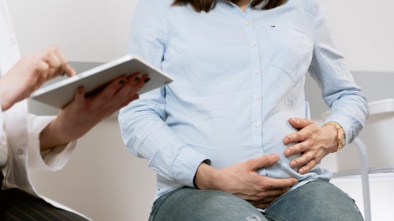 近距离的照片孕妇和她的手放在她的肚子上,医生穿白大褂的ipad。