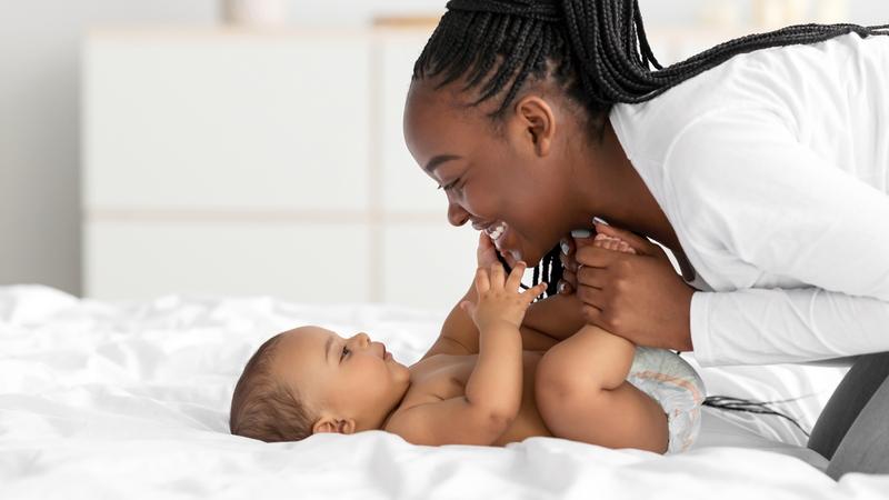 一个非洲裔美国人女人微笑着她的婴儿是谁在家躺在床上。