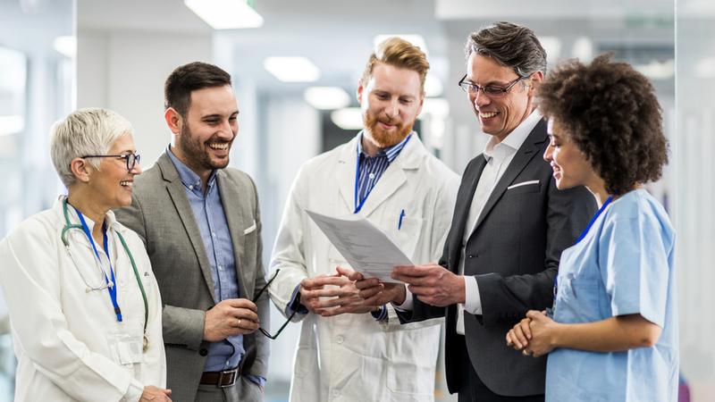 A group of professionals holds a standing meeting in an office setting.