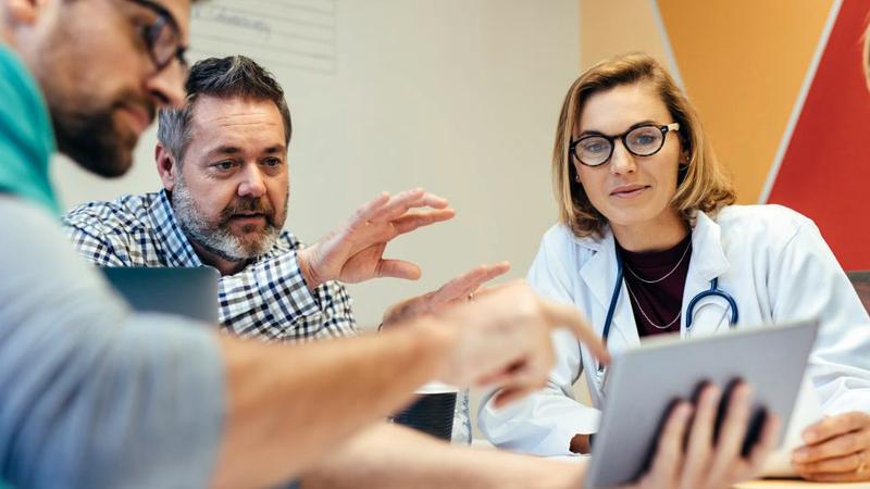 A group of doctors talk while looking at an ipad.