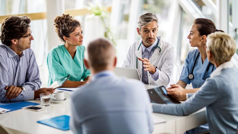 A group of medical professionals holds a meeting in a corner conference room office.