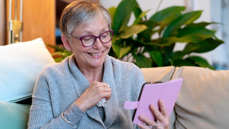 A senior woman smiles while having a telehealth visit on her phone.