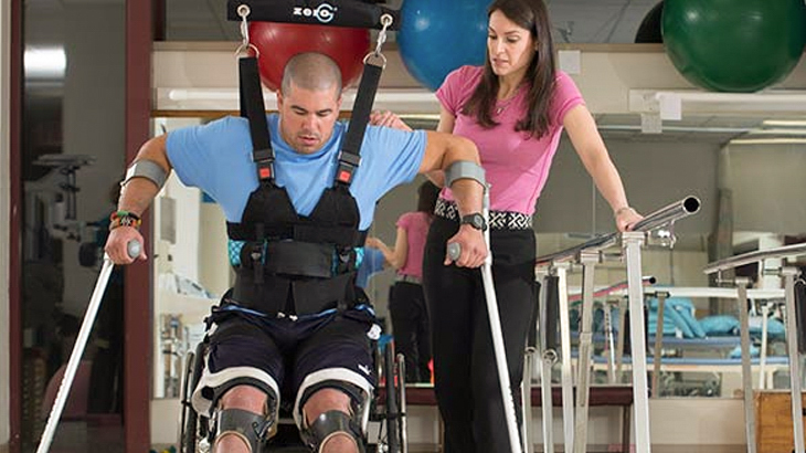A physical therapist works with a spinal cord/brain injury patient as he learns to walk with crutches and leg braces in the rehabilitation gym at MedStar National Rehabilitation Hospital.