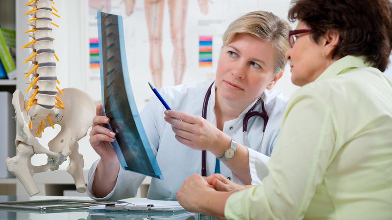 A doctor holds an xray film of a spine and talks with a patient.