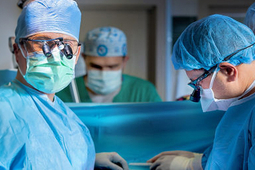 A surgeon wearing a blue mask looks at the camera.