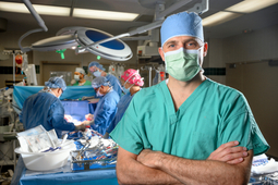 Dr. Christian Schults stands in an operating room while a surgical team works in the background.