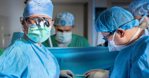 A surgeon wearing a blue mask looks at the camera.