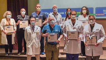 A group of faculty members from MedStar Health's Internal Medicine Residency in Washington DC stand together on a stage and hold their certificates. Everyone is wearing a mask.