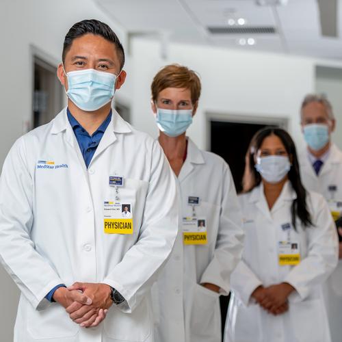 A group of 4 physicians stand in a line and pose for a photo in the hallway of a medical facility.