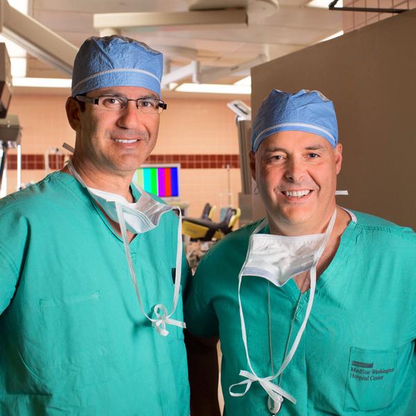 罗伯特·古特曼医生和詹姆斯·罗宾逊医生穿着绿色工作服，在MedStar华盛顿医院中心的手术室外合影留念。