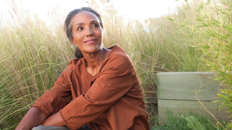 一个非裔美国人女人坐在草地上的高草,看上去这一边。
