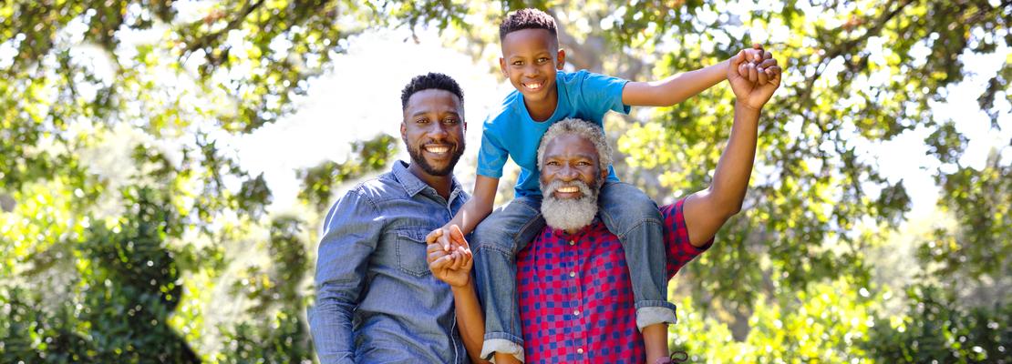 Multi-generation family enjoying their time at a garden. A small boy is sitting on his grandfather shoulders, looking at the camera and smiling