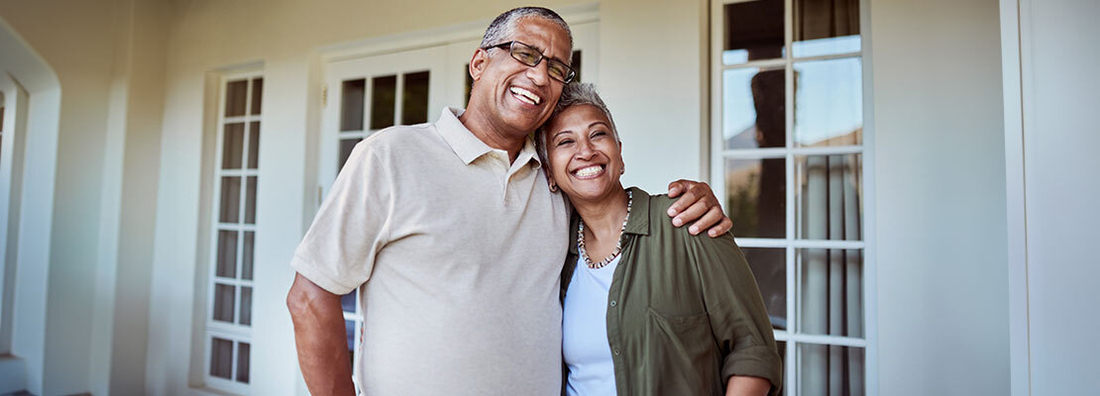 A couple stands together on the front porch of their home.